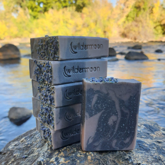 Lavender artisan soap with locally-sourced lavender essential oil. Rectangular bar soap with dark and light purple swirls with lavender buds on top and wildermoon logo stamp on side.
