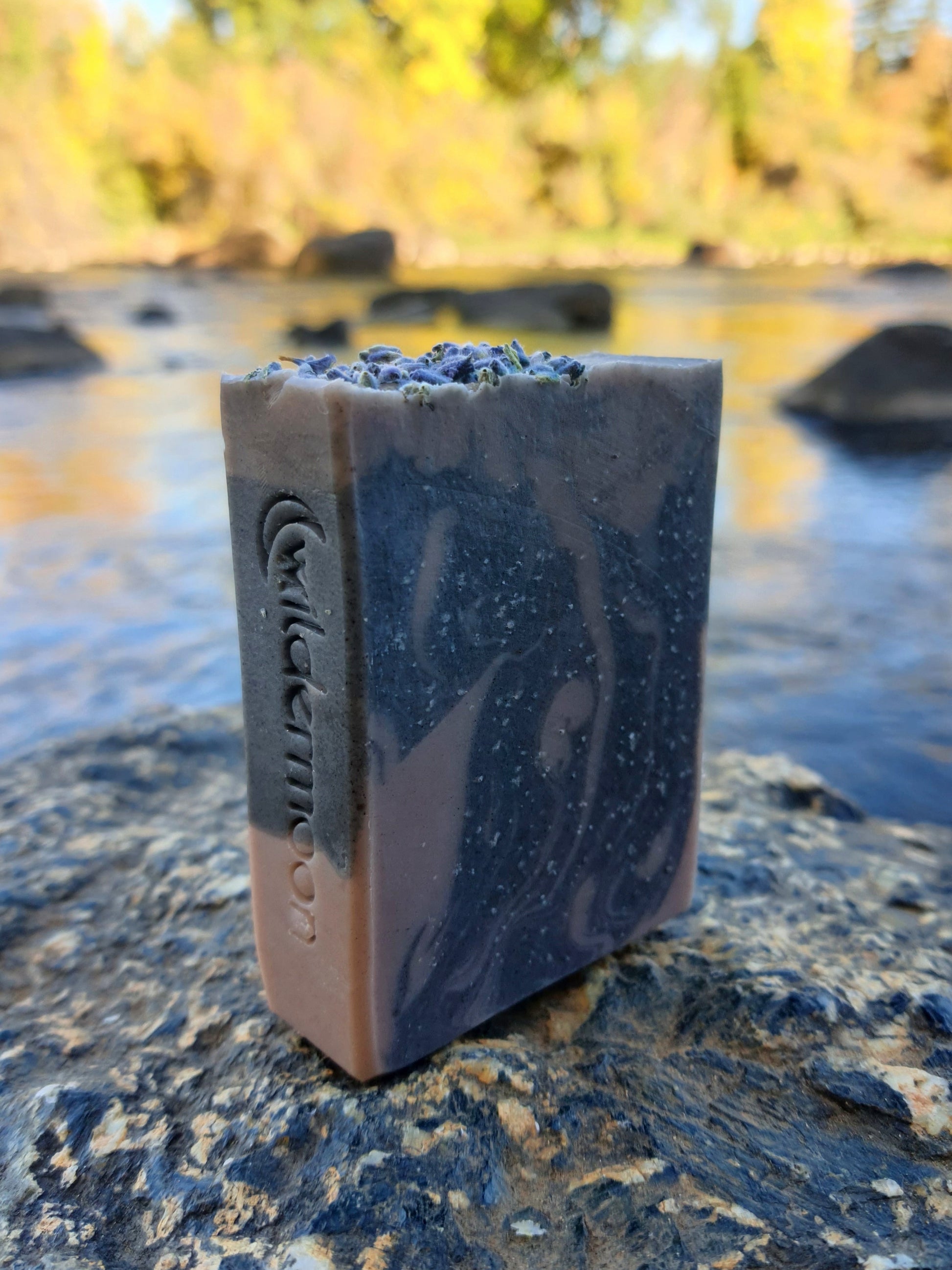 Lavender artisan soap with locally-sourced lavender essential oil. Rectangular bar soap with dark and light purple swirls with lavender buds on top and wildermoon logo stamp on side.